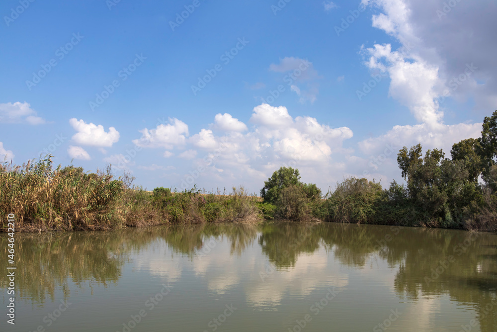 View of pond with trees around with clouds reflecting in the water.