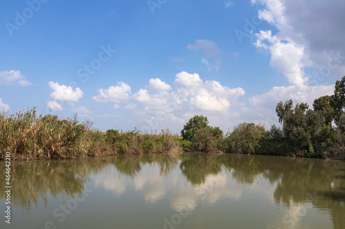 View of pond with trees around with clouds reflecting in the water. © Emma