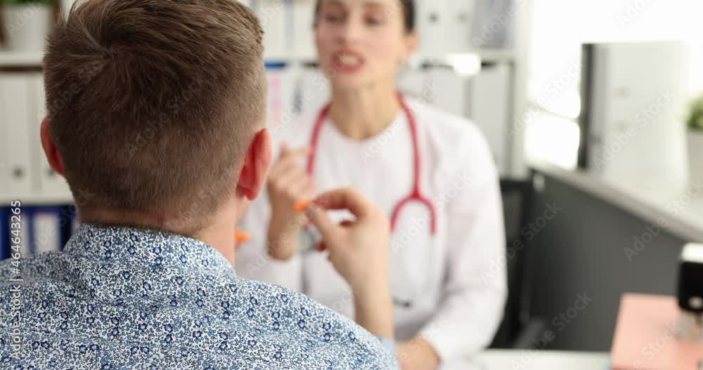 Male patient inserting earplugs into his ears while talking with doctor in clinic 4k movie Male patient inserting earplugs into his ears while talking with doctor in clinic 4k movie