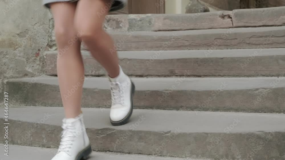 A woman quickly descends an old stone staircase in autumn white shoes. Female legs close-up A woman quickly descends an old stone staircase in autumn white shoes. Female legs close-up