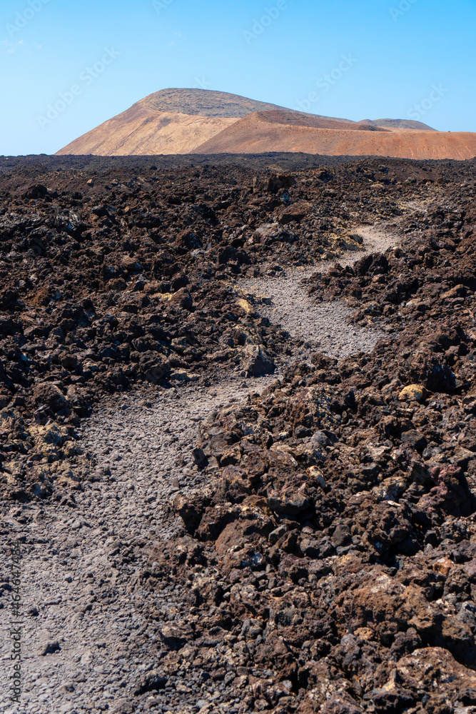 Path through old lava to a volcano in Lanzarote, Canary islands, Spain. Volcanic landscape.