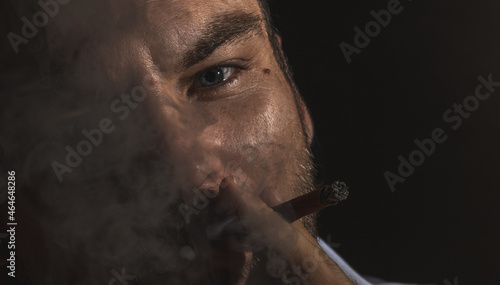 The adult man smokes a cigar, face in smoke extremely close-up.