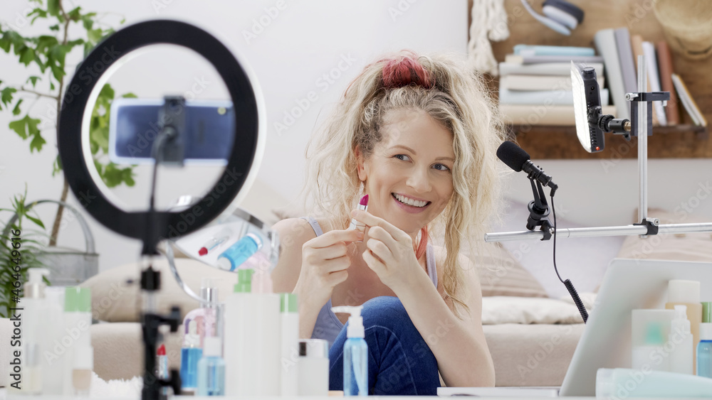 Blonde smiling woman influencer blogger recording a video tutorial on  smartphone camera showing lipstick. Female vlogger making a beauty vlog for  makeup products her online internet channel. foto de Stock | Adobe