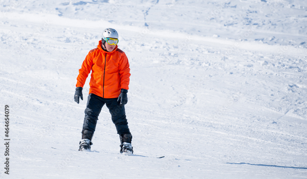 A snowboarder in a ski resort rides on a slope of snow-capped mountains. Winter kind of leisure, sporty lifestyle.