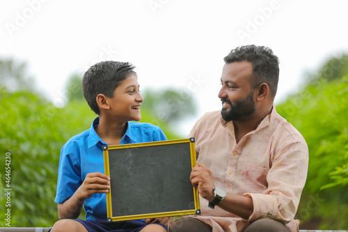 education concept : young indian farmer showing blank chalkboard with his child