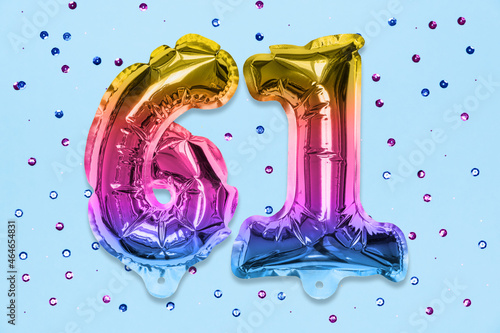 Rainbow foil balloon number, digit sixty one on a blue background with sequins. Birthday greeting card with inscription 61. Top view. Numerical digit. Celebration event, template. photo