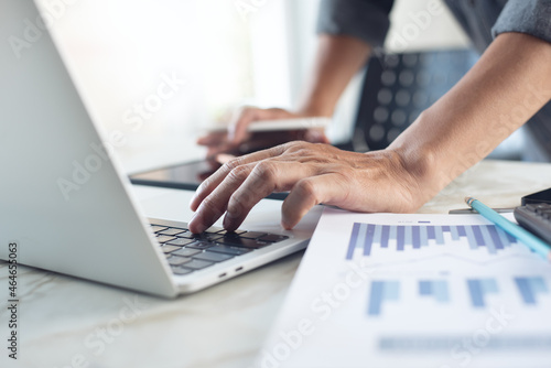 Business man working at office with laptop computer and digital tablet and financial report graph data documents on his desk, close up