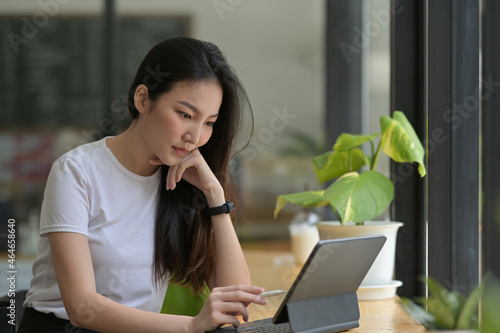 Photo of beautiful woman keep a hand on chin while using a digital tablet and stylus pen at the wooden counter. photo