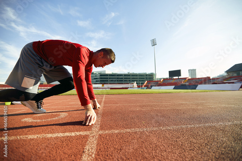 image of young adult caucasian male athlete in low start position at athletic track.