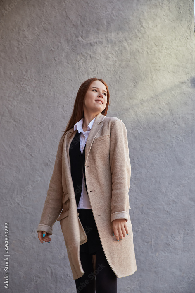 beautiful young caucasian red headed woman in beige coat with long hair standing outdoors in front of wall. attractive female street portrait at fall. autumn lifestyle, stylish fashion outfit beautiful young caucasian red headed woman in beige coat with long hair standing outdoors in front of wall. attractive female street portrait at fall. autumn lifestyle, stylish fashion outfit