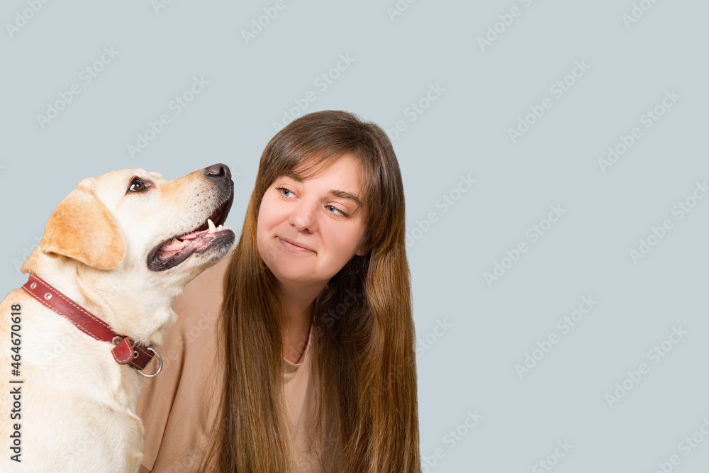 Portrait of a young beautiful girl with long hair and a labrador dog, on a blue background. The image has a blank space for your text. Portrait of a young beautiful girl with long hair and a labrador dog, on a blue background. The image has a blank space for your text.