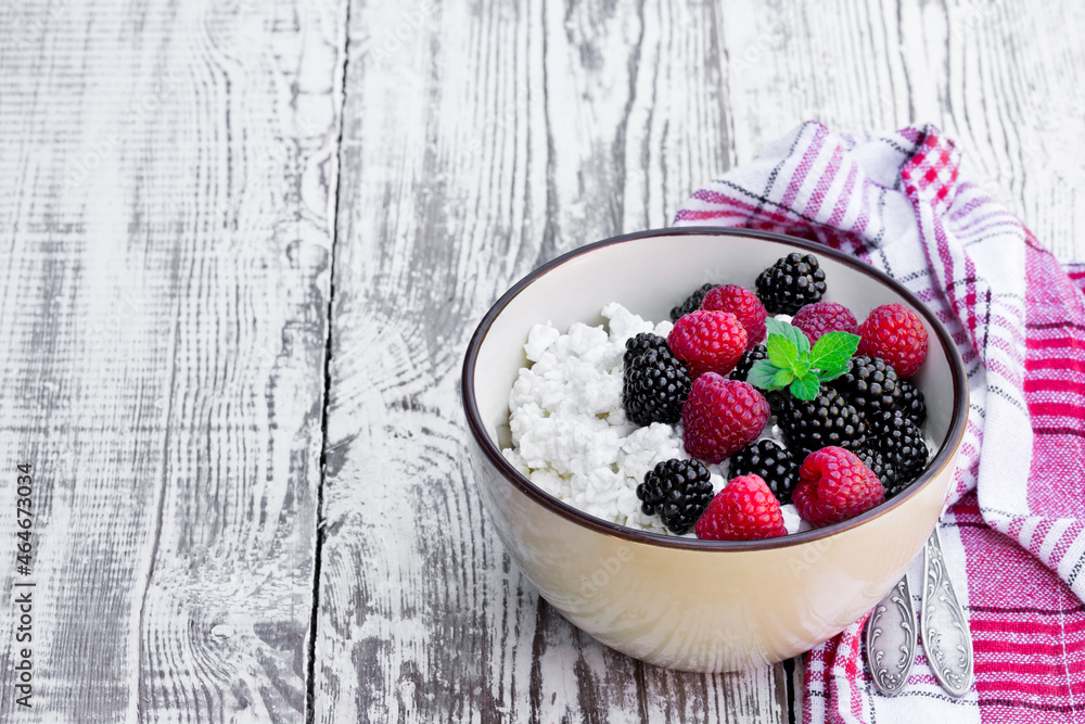 Cottage cheese with fresh raspberry and blackberry in ceramic bowl on white wooden table