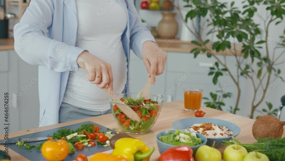 Pregnant Woman Preparing Organic Healthy Food. The Woman Mixes Vegetable Salad in a Bowl in the Kitchen. Healthy Vegetarian and Vegan Diet Concept. Pregnant Woman Preparing Organic Healthy Food. The Woman Mixes Vegetable Salad in a Bowl in the Kitchen. Healthy Vegetarian and Vegan Diet Concept.