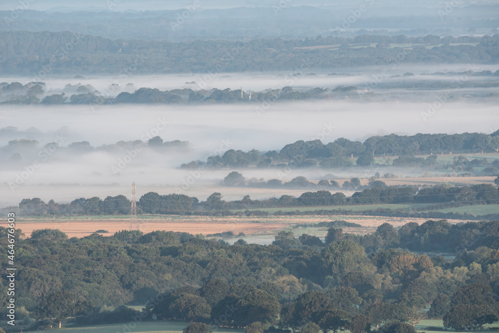 Beautiful foggy morning landscape image looking across fields on the South Downs National Park in rolling English contryside during late Summer