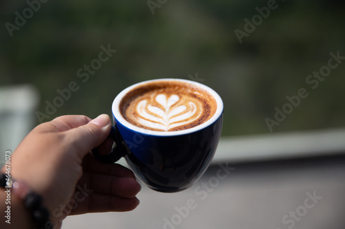 cup of cappuccino with latte art holding by woman with mountain view background