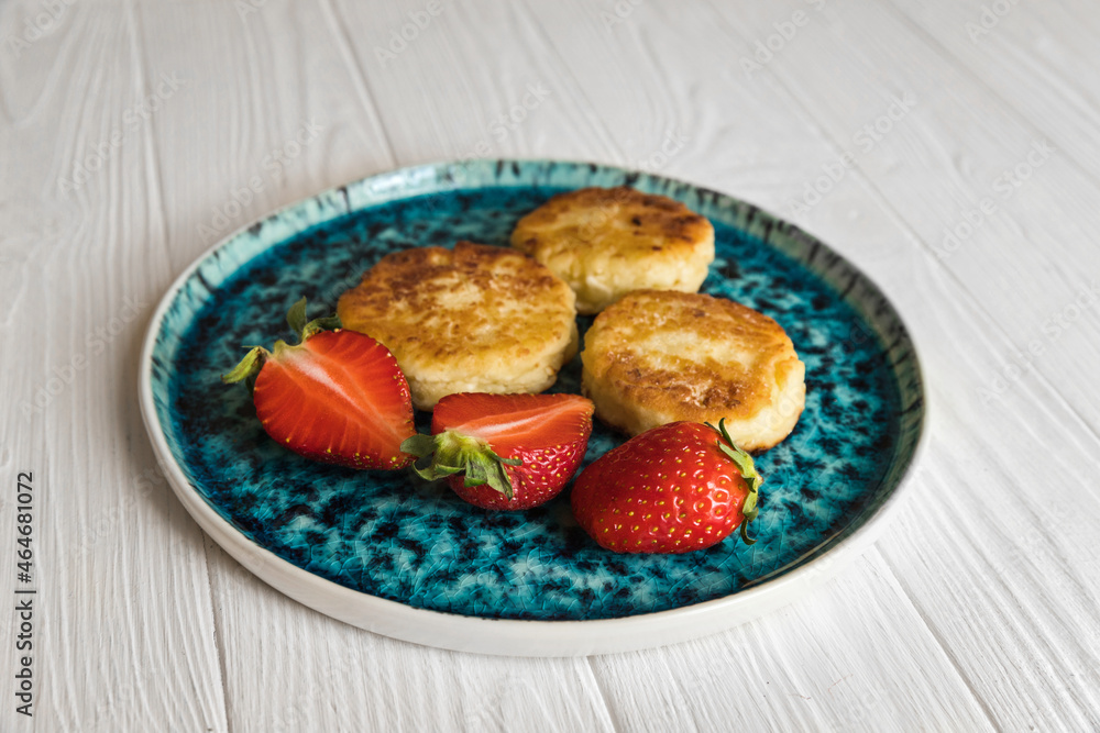 Сheese pancake, сheesecakes with fresh strawberries on a blue plate on a white wooden table background Сheese pancake, сheesecakes with fresh strawberries on a blue plate on a white wooden table background
