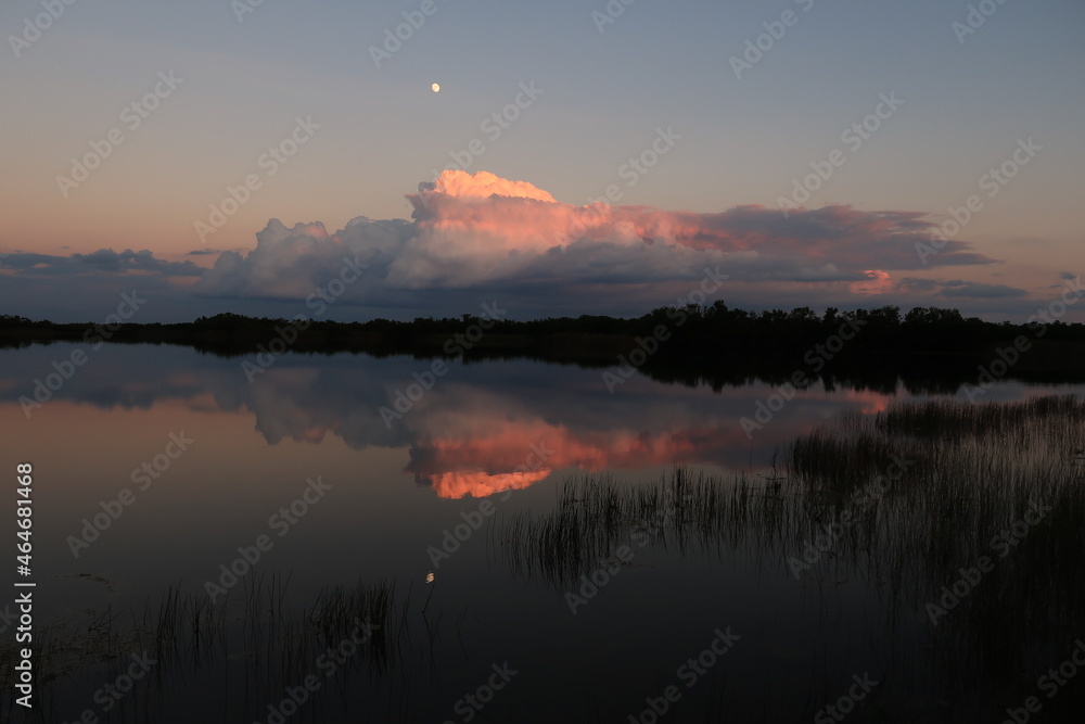 Moonrise over colorful autumn clouds reflected on calm water of Nine Mile Pond in Everglades National Park, Florida at sunset.