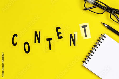 Content word with eyeglases and notebook on yellow background, flat lay photo