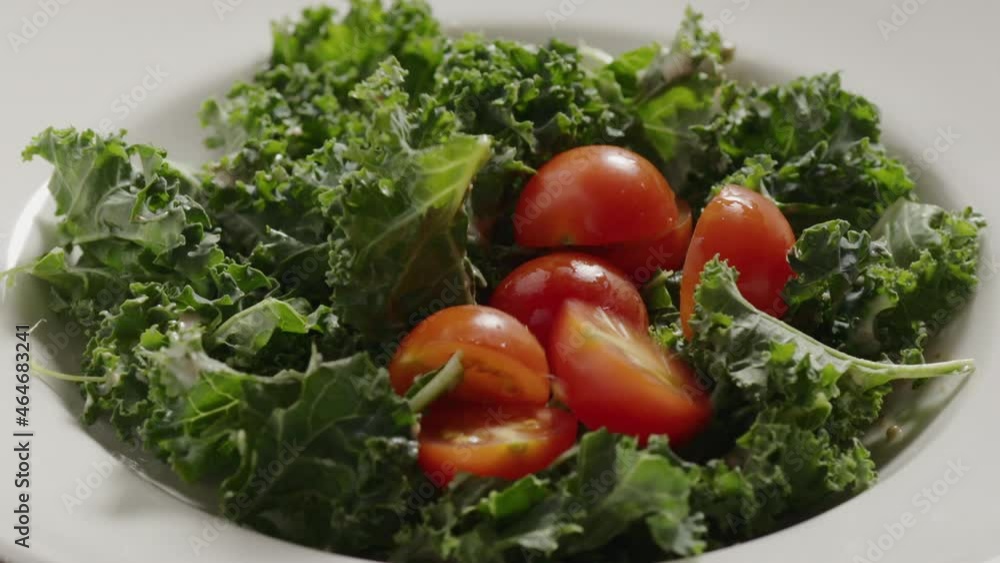 Slow motion cherry tomatoes fall on kale leaves on white plate Slow motion cherry tomatoes fall on kale leaves on white plate