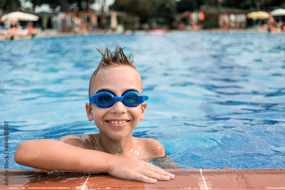 Boy in blue goggles for swimming in the pool. Summer vacation of a child in the pool.