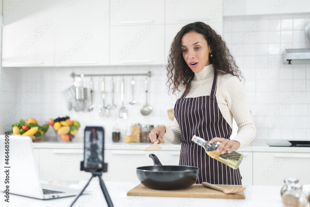 Latin women live streaming online with a smartphone while cooking in the kitchen at home. Latin women live streaming online with a smartphone while cooking in the kitchen at home.