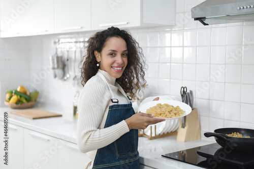 A portrait of a smiling Latin woman enjoying cooking is in the kitchen. Healthy lifestyle, food, diet concept.