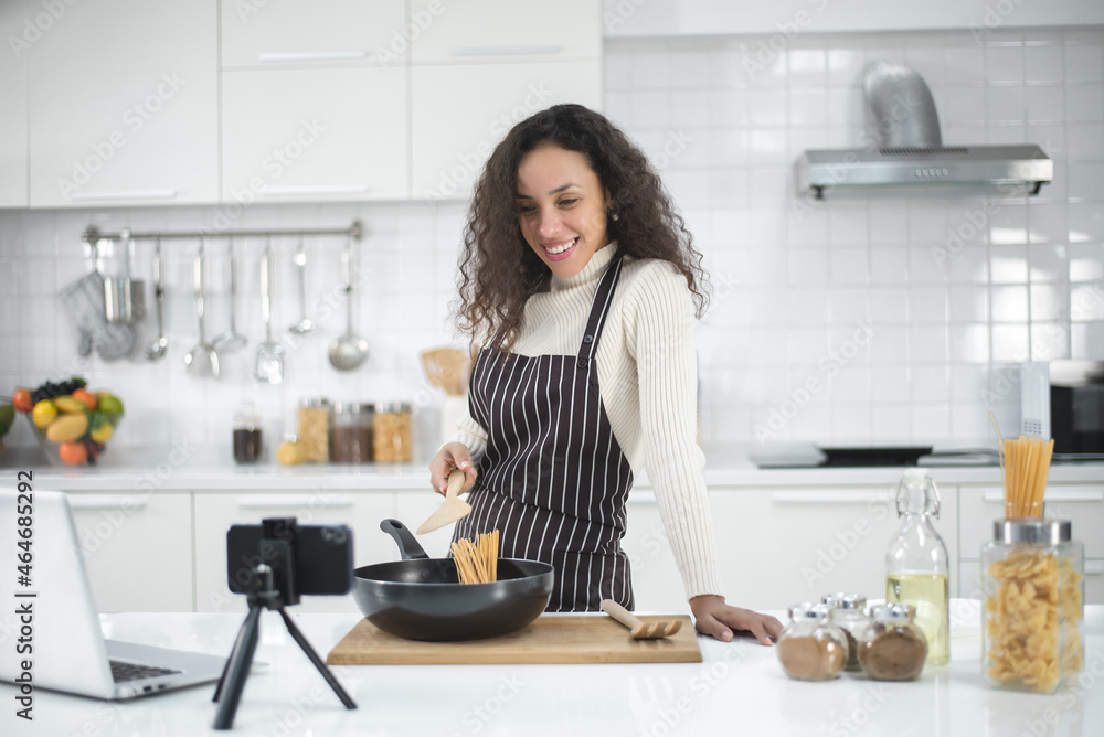 Latin women live streaming online with a smartphone while cooking in the kitchen at home. Latin women live streaming online with a smartphone while cooking in the kitchen at home.
