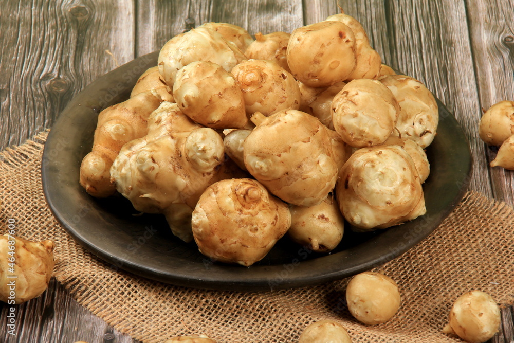 Raw Jerusalem artichoke in a clay bowl on wooden boards background. Raw Organic topinambour Raw Jerusalem artichoke in a clay bowl on wooden boards background. Raw Organic topinambour