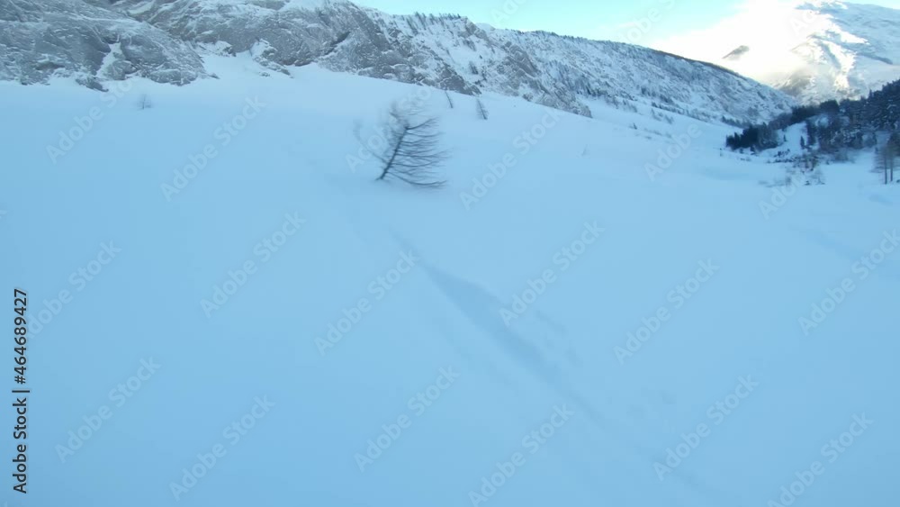 Point of view shot of a man, in a yellow ski jacket, snowboarding on a ski resort, while sun illuminating a mountain top in the background Point of view shot of a man, in a yellow ski jacket, snowboarding on a ski resort, while sun illuminating a mountain top in the background