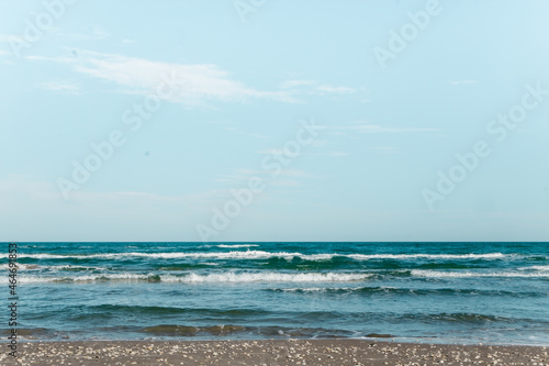 mid-day beach scene with small waves crashing on the beach and many small shells at the shore