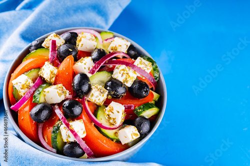 Greek salad and blue napkin on a blue background. Fresh vegetables, feta cheese and black olives. Greek cuisine. Top view. Copy space