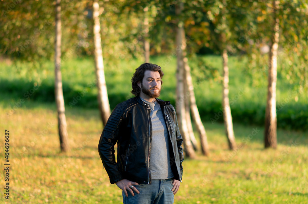 Young bearded man standing and looking at distance against a background of colorful autumn trees Young bearded man standing and looking at distance against a background of colorful autumn trees