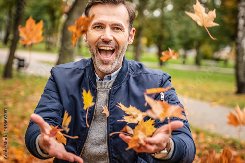 Handsome man is having fun  playing throwing leaves in the autumn park