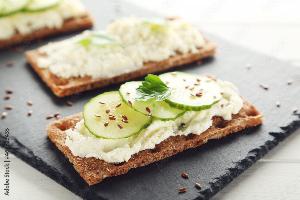 Crispbread with cream cheese and cucumbers on white wooden table
