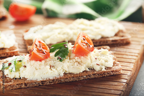 Crispbread with cream cheese, tomato and green parsley on brown board