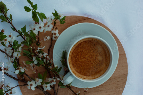 A cup of coffee  a book and blooming cherry branches on a white tablecloth. White sakura. Atmosphere  comfort  rest