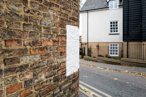 Large painted white marker seen on the side of an old wall to a house. Located on a narrow, sharp bend in an English city centre, to help prevent vehicles hitting the wall.