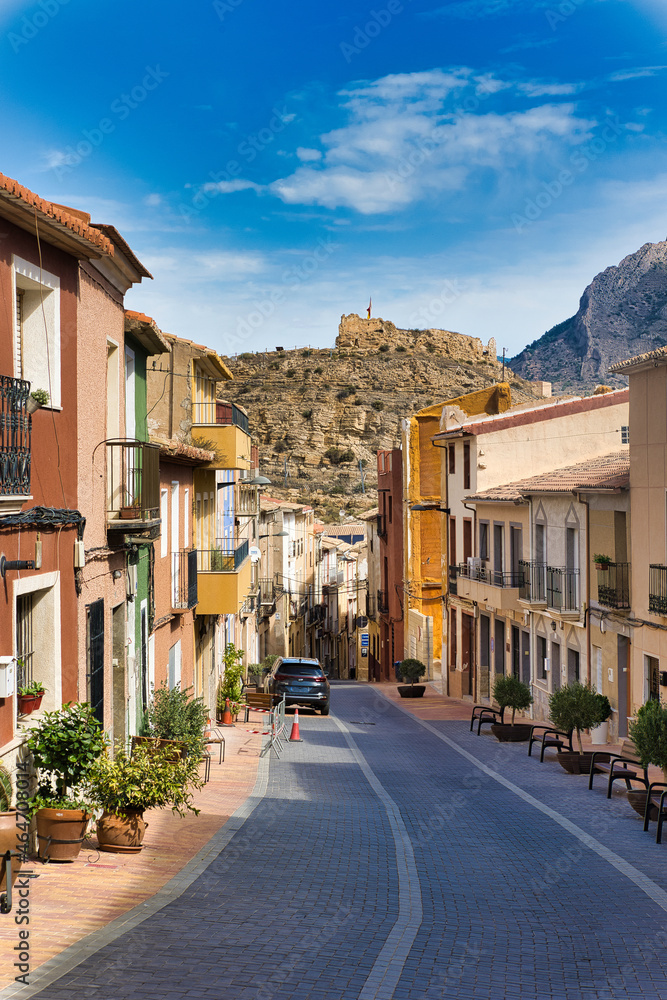 Busot in Spain, Alicante province. Historical, characteristically narrow street overlooking a hill with castle ruins. Vertical view.