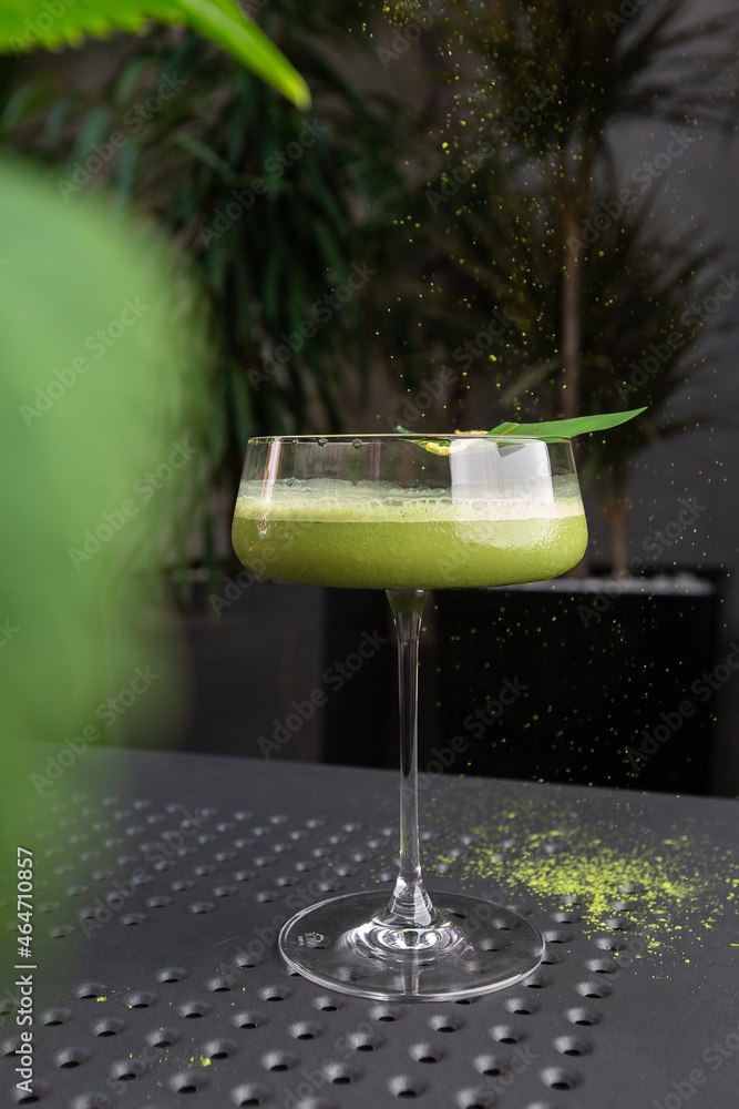 Glass with green matcha sour cocktail decorated with green leaf on background with pink flovers