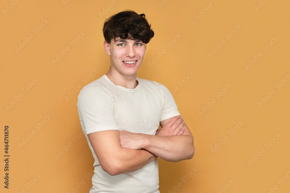 Handsome teenage boy in white t-shirt smiling happily on yellow background. The guy has healthy white teeth, the concept of beauty and health in adolescence Handsome teenage boy in white t-shirt smiling happily on yellow background. The guy has healthy white teeth, the concept of beauty and health in adolescence