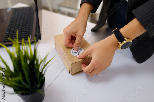 Female hands sticking a logo label on carton, paper box. Potflower on white table background.