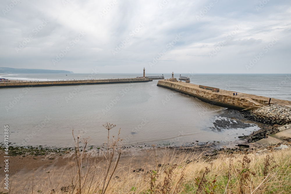 Whitby, Yorkshire, UK – October 18 2021. A wide angle shot of the East and West piers, and their respective lighthouses of Whitby Harbour from high above