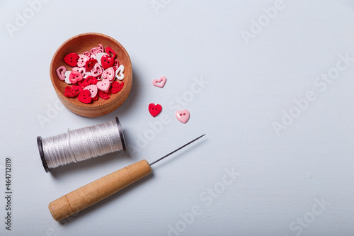 Wooden bowl of heart shaped red and pink buttons with spool of threads and awl for sewing and embroidery on white background. Set of materials for handcraft, making of bijouterie and accessories.