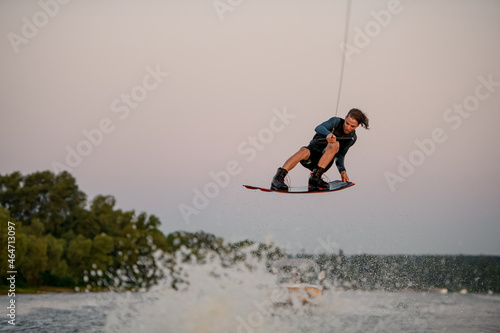 energy man flying over splashing wave on wakeboard holding on to the rope photo