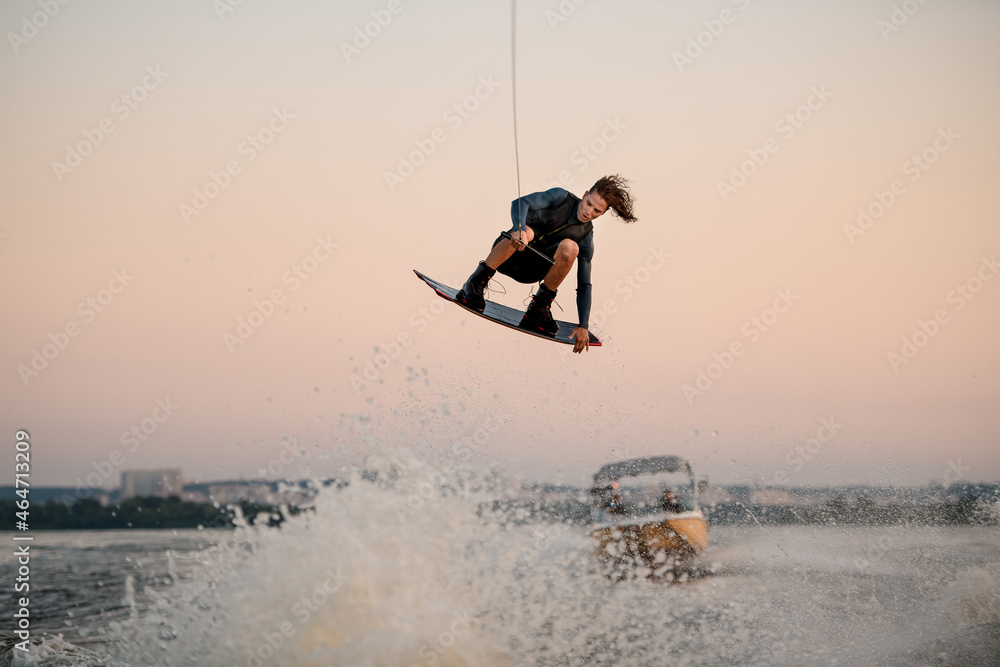 active athletic man flying over splashing wave on wakeboard holding on to the rope