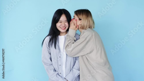 Woman gossip. Secret share. Female friendship. People diversity. Multiracial girls friends whispering rumor hearsay laughing on blue free space background. photo