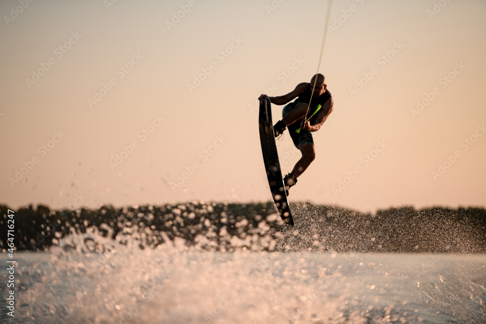 muscular man making trick in jump time with wakeboard against the backdrop of the sky