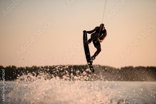 muscular man making trick in jump time with wakeboard against the backdrop of the sky photo