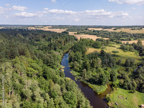 Areal landscape view of small countryside river flowing through agriculture field and forest.