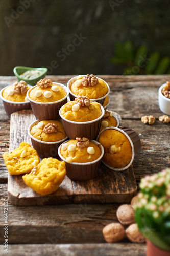 Pumpkin muffins with white chocolate and walnuts. Side view, wooden and green background.